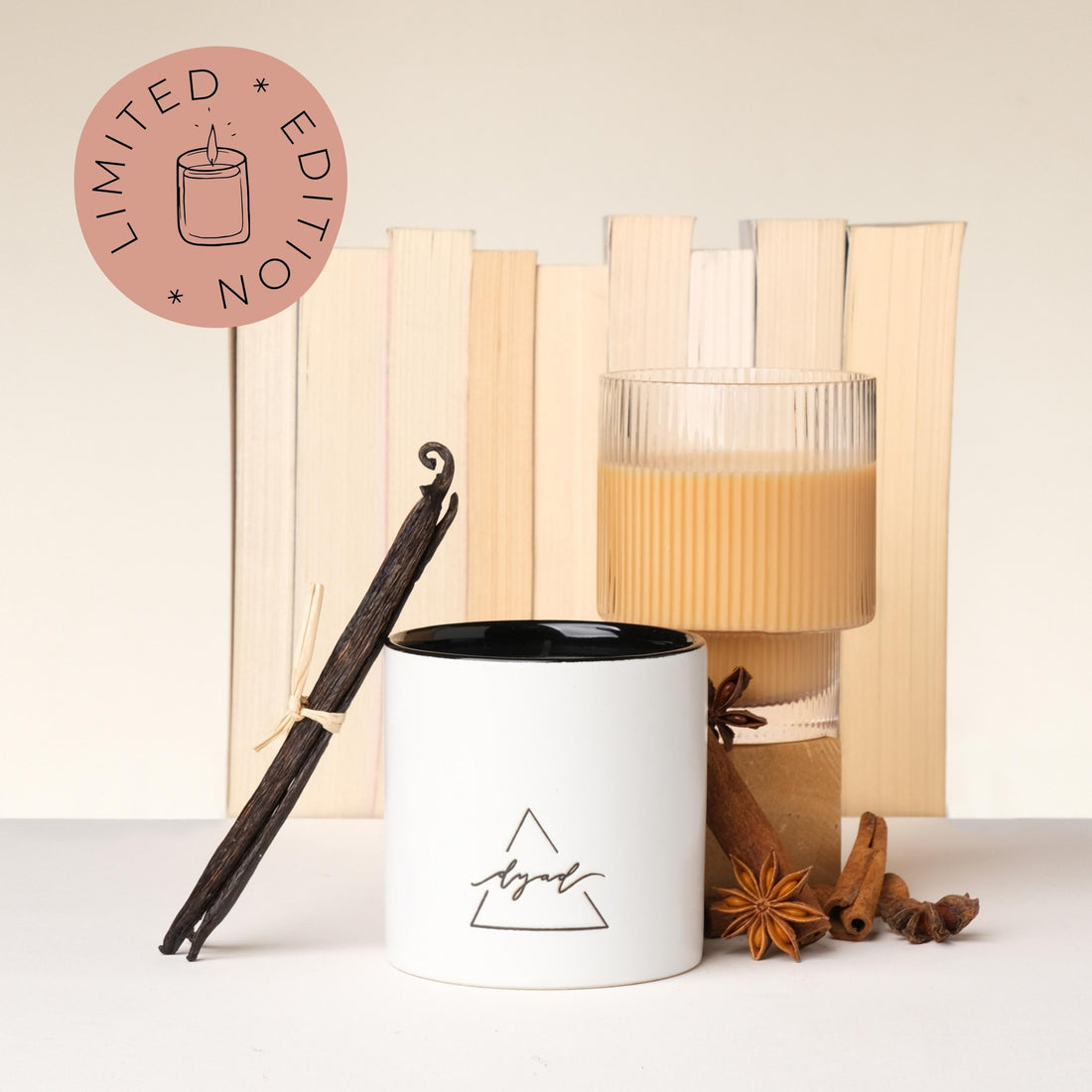 candle displayed with books, cinnamon sticks, star anise, vanilla bean, and a chai latte